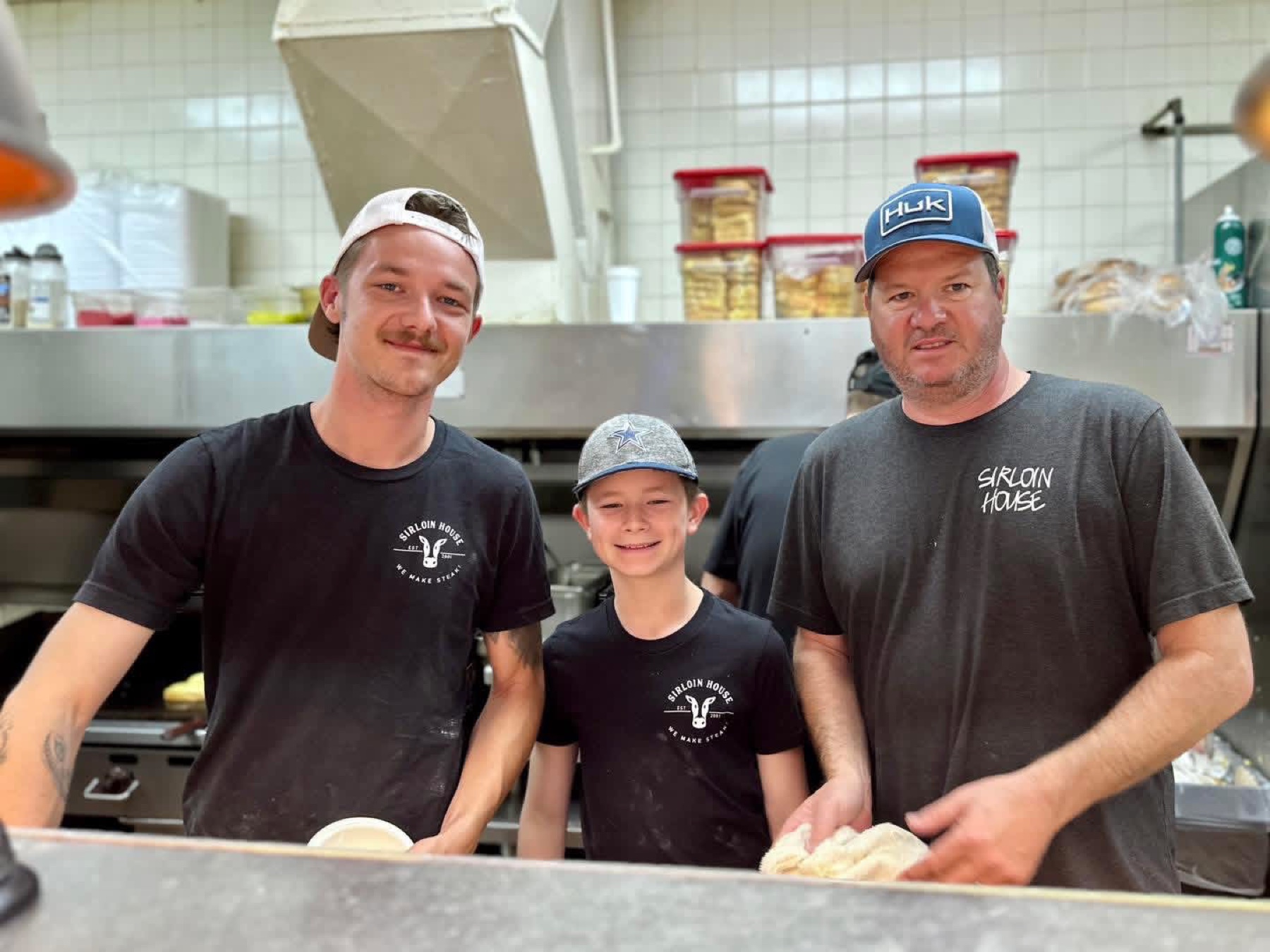 Three generations of family in the kitchen at The Sirloin House — the hands behind every plate that goes out the window